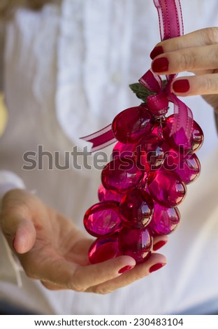 Woman with elegant white blouse holding in her hands a beautiful bunch of red grapes made of glass for Christmas decoration.