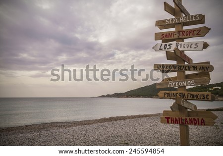Wooden post with many written signs of different destinations in all directions, in a cloudy day,  Cala Codolar, Ibiza, Balearic Islands, Spain