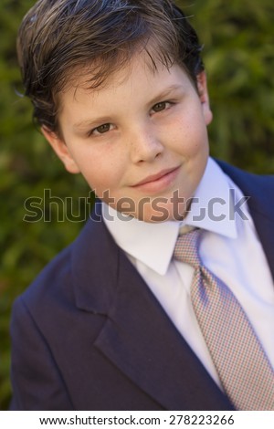 Color portrait of ten year old boy dressed in dark blue suit and tie for his first communion with green leaves background.