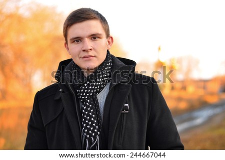 Portrait handsome young man in coat outdoors in autumn park