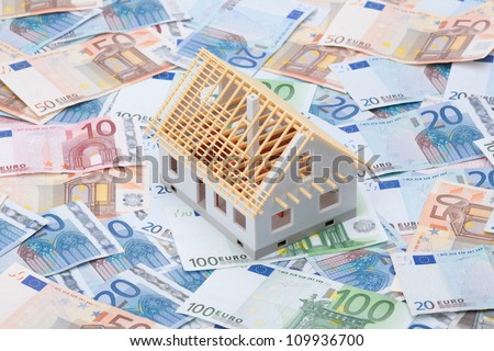 Building cost (construction cost) concept. Model of house under construction (rough construction) and money.