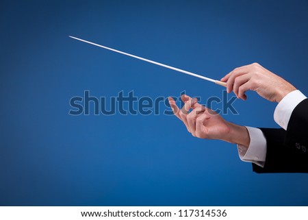 Male orchestra conductor hands, one with baton. Blue background.