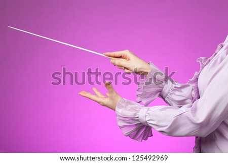 Female orchestra conductor hands, one with baton. Pink background.