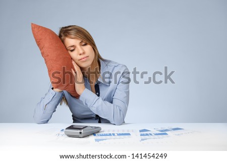 Woman having a rest (sleep, relax, snooze, nap, doze) in work. Burnout tired worker. Weary woman with pillow, graphs, sheets and calculator.