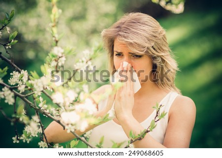 Woman with pollen allergy in springtime near tree in bloom.