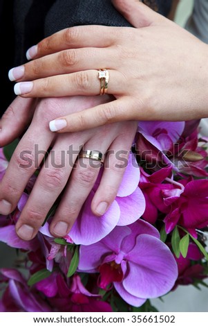 Wedding Rings and Hands Over Bridal Bouquet