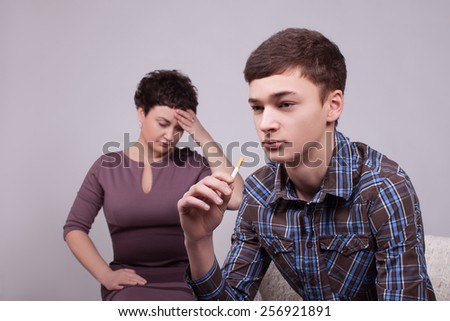Difficult teenager . Young guy with a cigarette in hand, his mother took his head, crying
