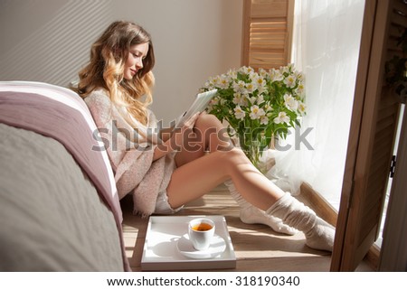 sun is shining into the bedroom,she looks out the window. Long beautiful legs.lady sitting next to the bed,woman in the morning to read electronic books.Morning coffee,enjoyment,she closed her eyes