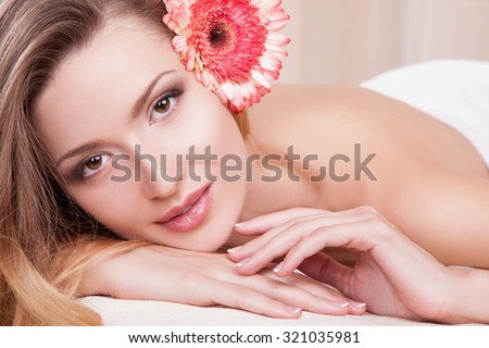Portrait of a woman at a spa salon, she was without clothes covered with a towel.Woman and spa.Beautiful portrait woman in her hair pink flower,brown eyes looking straight at the camera. beauty.