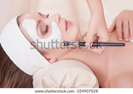 Elegant woman with perfect skin on her face,the girl with eyes closed receiving beauty treatments.Girl with dark hair lying on her back in the beauty salon.Beauty.Female face with a white mask.