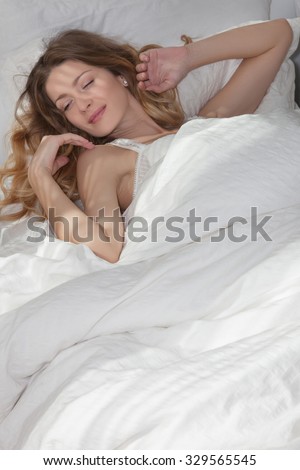 Beautiful girl sleeping in the early morning in my warm cozy bed, she wakes up and smiles.   Woman lying on the back in white bed 6, the sun shines on the bed through the blinds.