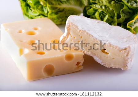 Two different kinds of cheese - camembert and edam with big holes laying near to small roman lettuce