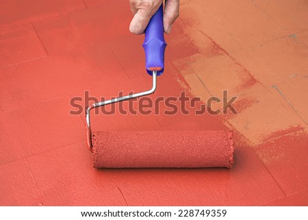 Hand painting a red floor with a paint roller for waterproofing