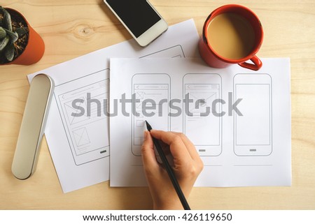Designer drawing mobile application wireframe on wooden desk. Top view