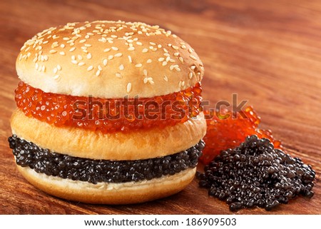 Burger with salmon roe. Sandwich with black caviar and salmon caviar on wooden table
