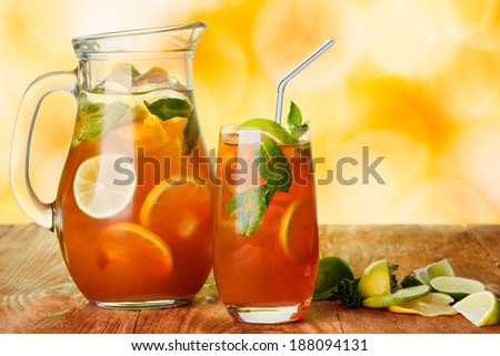 Iced tea in the pitcher and the glass.  Jug of cold iced drink with lemon and mint on wooden table over abstract background