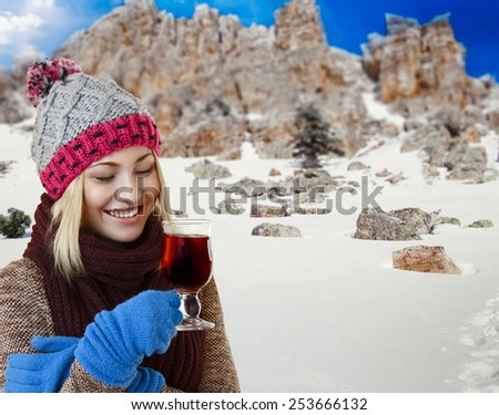 Attractive smiling woman holding a cup of tea, punch or mulled wine against winter mountain background