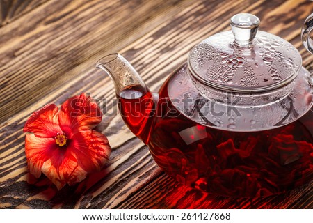 Hibiscus tea in transparent teapot on wooden table. Worldwide popular healthy tea known as rosella, karkade or red sorrel.