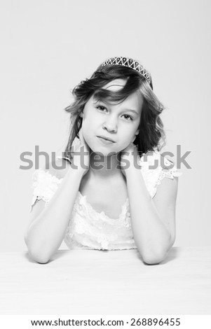 Young thoughtful girl wearing white lace dress and diadeam sitting at the white table