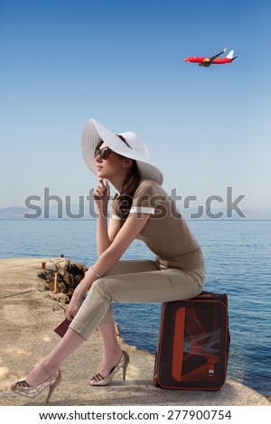 Traveling stylish woman sitting on her luggage on the pierce near the sea while holding her passport and dreaming. Travel,vacation,tourism concept.