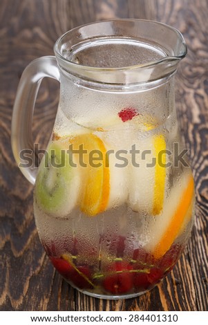 Glass pitcher of homemade detox water enriched with cherries and frozen fruit wedges. Misted jug full of cold water with popsicles. Clean eating