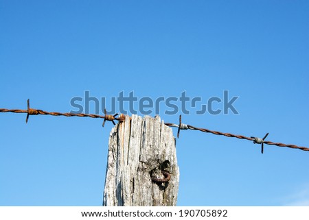 Single strand of barbed wire supported on a wooden fence post.