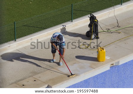 A worker is cleaning a swimming pool with a brush