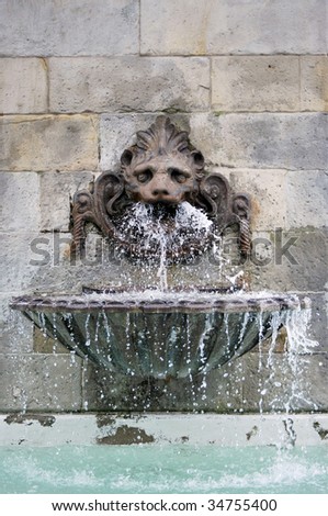 Antique fountain in a wall. Water is flowing from the mask