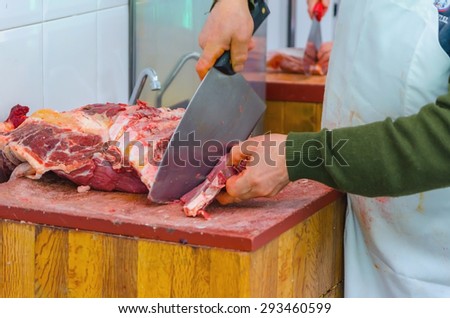 A butcher cuts a piece of raw meat with the knife