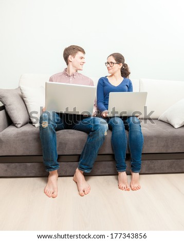 Young man and woman sitting on couch with laptops and looking at each other