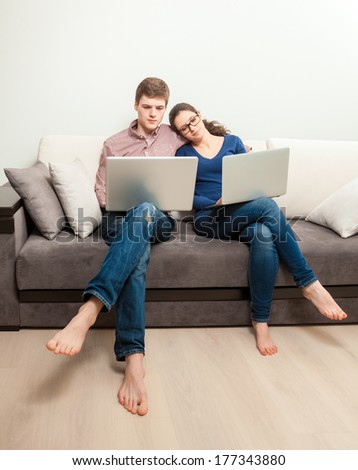 Young couple in love sitting on couch and using two laptops