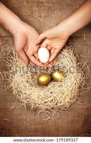 Conceptual photo of men and women hands putting white egg to nest with two golden eggs