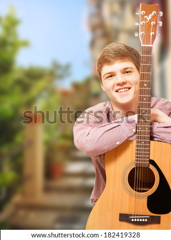 Closeup portrait of handsome young guitarist posing against summer street view