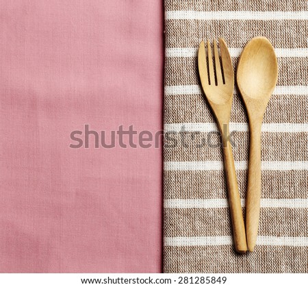 Wooden spoon and fork on pink towel and wood board background