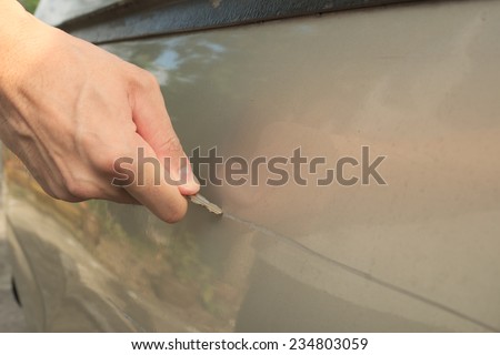 Male hand scratching a car by using silver key