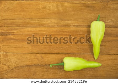 Two hot green chili pepper forming right angle over wooden background