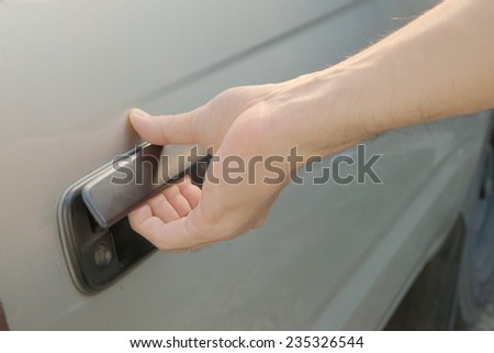 Male hand opening car door from outside by pulling black plastic door handle