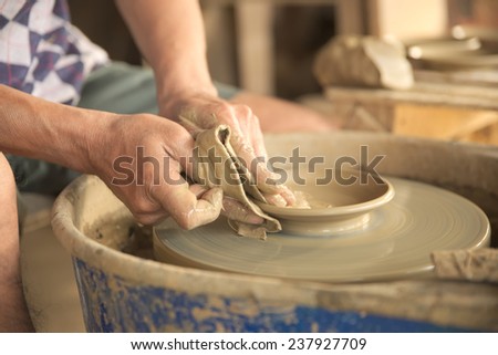 Old Thai male hand shaping a gray color clay dish by using a cotton cloth.