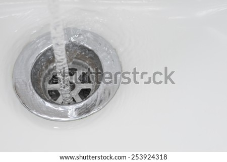 Closeup of tap water flowing into stainless steel drain of white washbasin background