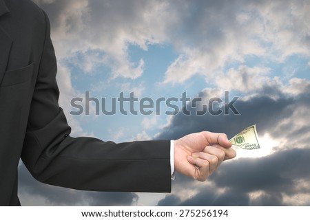 Business man donate 100 dollar note over bright overcast sky with sun light leak out of cloud