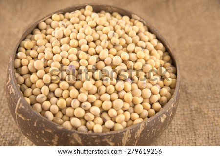 Wooden bowl filled with full size yellow beans over agriculture sack background