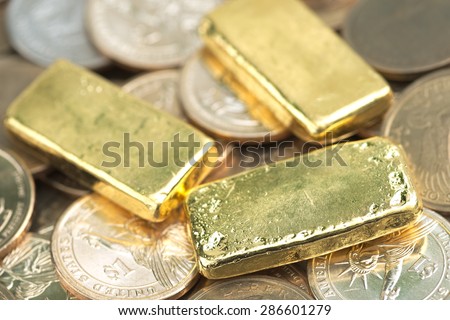 Stack of actual smallest gold bar commonly sold in Thailand over pile of dollar coins. Each bar is 96.5% purity gold which roughly equals to 99.5% purity 2.527 troy ounce.