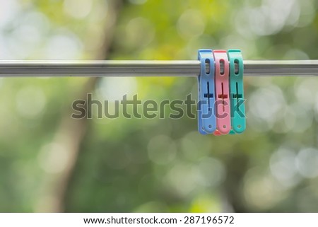 Blue, green, and pink cloth pegs hanged on stainless steel clothesline back lit over green natural bokeh background