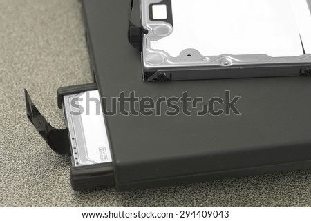HDD partially pop out of black laptop slot with another HDD on top of laptop over working desk