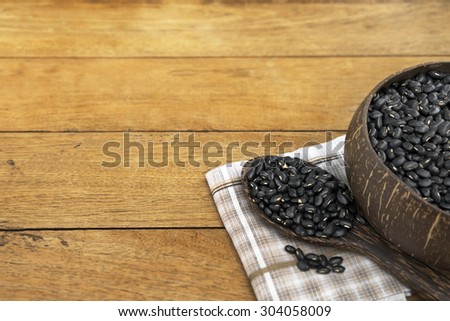 Part of bowl fully filled with black bean and a focused spoonful of black bean on napkin over wooden table.