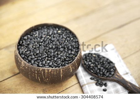 Shallow DOF of bowl fully filled with black bean and a spoonful of black bean on napkin over wooden table.