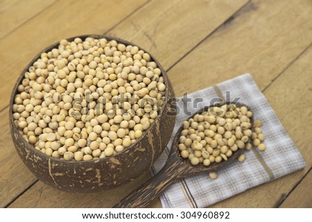 Wooden bowl filled with full size yellow beans and a spoonful of bean over napkin on top of wooden table