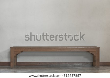 Empty long wooden chair in front of plain yellow rough surface concrete wall