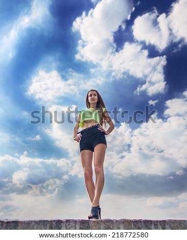 Beautiful fitness girl with perfect legs on the blue sky background with clouds