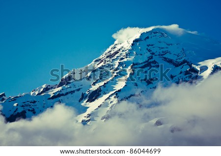 closeup of summit of a snow capped mountain while a cloud forms at the summit.
